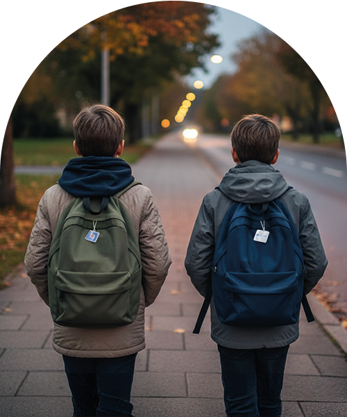 Tv&aring; pojkar sedda bakifr&aring;n g&aring;r p&aring; en trottoar i skymningen med ryggs&auml;ckar, varav b&aring;da har en liten reflex.
